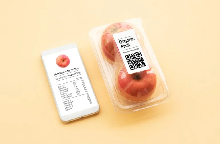 Smartphone showing nutrition facts for an apple beside a plastic container of organic fruit with a QR code label.