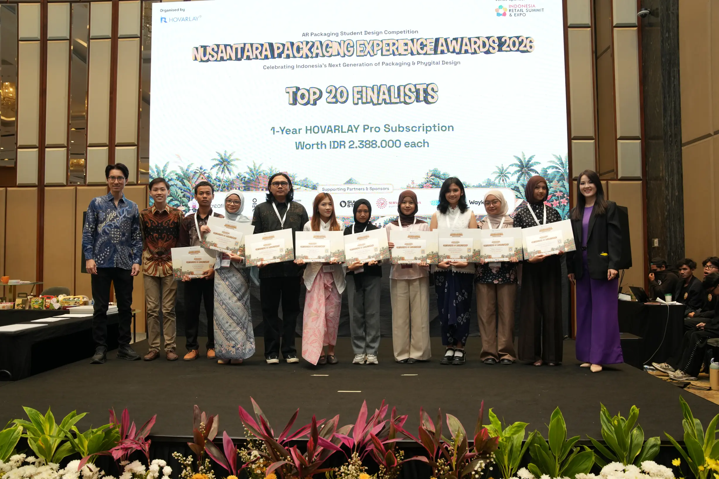 Group of finalists and organizers on stage holding certificates at the Nusantara Packaging Experience Awards 2026 ceremony. Behind them is a large screen displaying the event name and graphics.